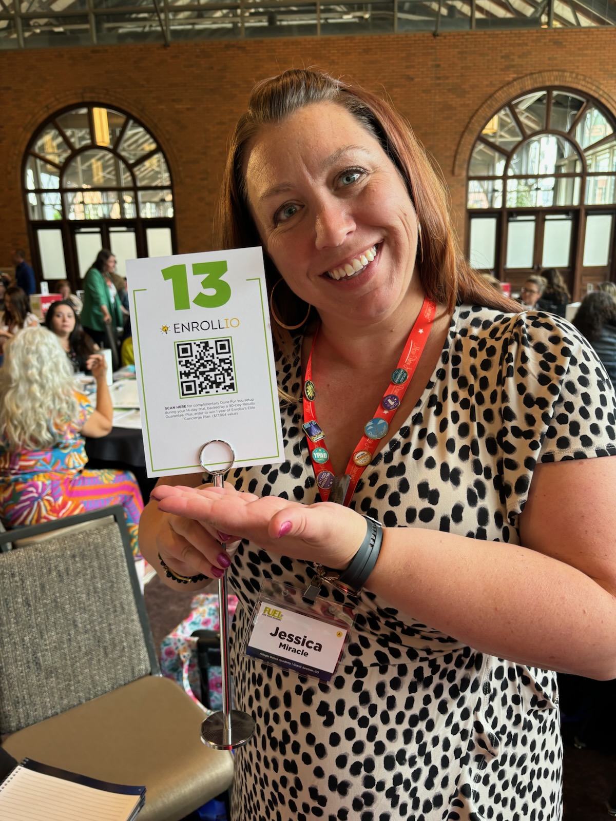 Studio owner smiling while holding an Enrollio table card at an industry event